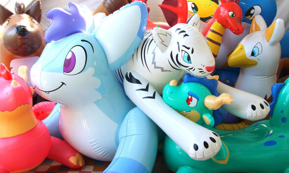 A large pile of inflated pool toys of many styles, including a white tiger, a large blue rabbit, green and red dragons, a griffin, and a hyena.